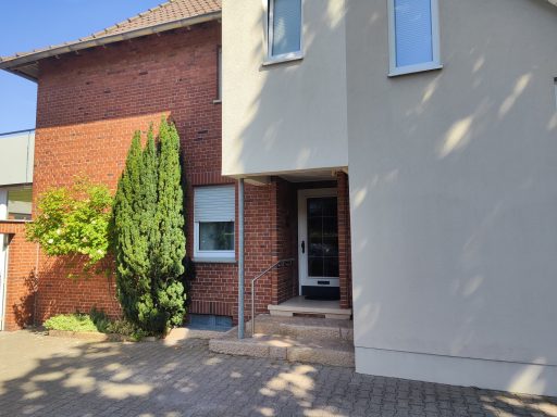 Eingang zu einem Wohnhaus mit einem kleinen Garten und einer Zypressenhecke.