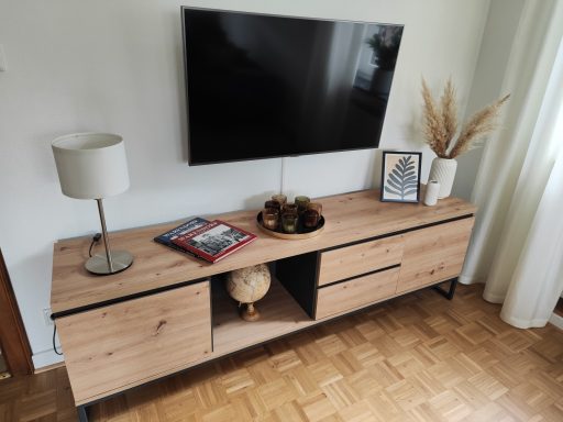 Moderne Wohnwand mit Fernseher, Lampe, Dekoration und Zeitschriften auf einem Holzschrank.