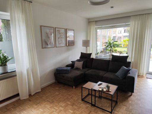Moderner Wohnbereich mit schwarzem Sofa, Beistelltisch und Pflanzen neben einem großen Fenster.